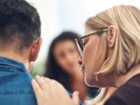 Eine Frau spricht mit einem Mann und legt ihm dabei die Hand auf die Schulter.